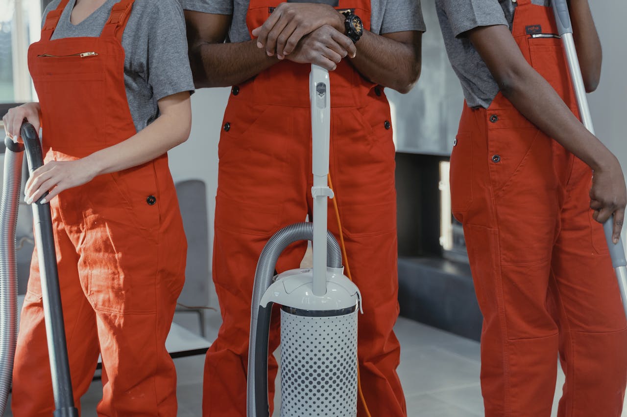 why-choose-us Three workers in red coveralls with cleaning tools in a room.