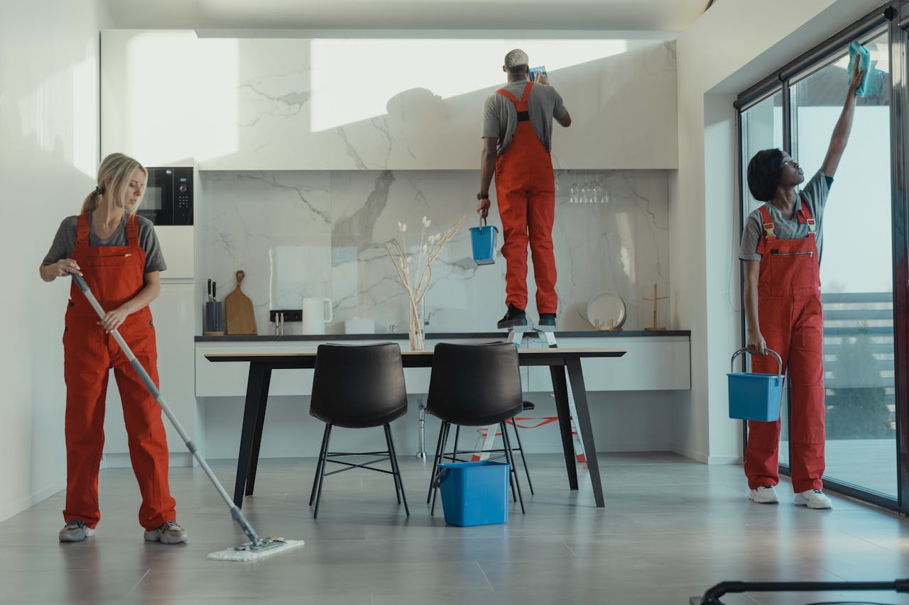 contact-img Group of cleaners in red uniforms mopping and wiping glass in a modern dining room.